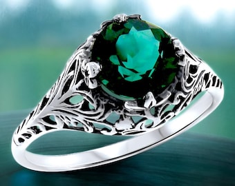 May include: A silver ring with a green gemstone set in a filigree design. The ring has a delicate, intricate design with a floral motif.