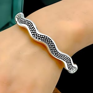 May include: A silver bangle bracelet with a wavy design and a textured surface.