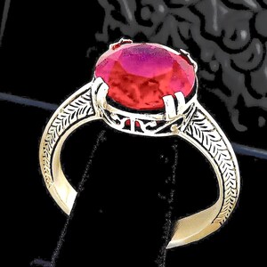 May include: A silver-toned ring featuring a large, round, faceted vibrant pink gemstone held by four prongs. The band is crafted with a detailed, etched leaf-like pattern along the sides, leading up to an openwork metal gallery setting.