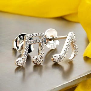 May include: Silver musical note earrings with clear cubic zirconia stones. The earrings are a classic design and would make a great gift for a music lover.