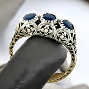 May include: A silver ring with three dark blue gemstones set in a floral design.