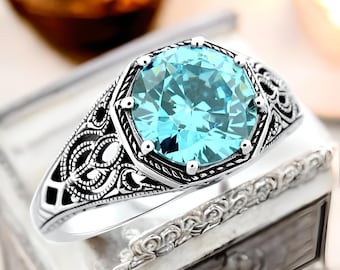 May include: A silver ring with an ornate design and a large, round, light blue gemstone.