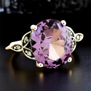 May include: A gold ring with a large, oval-shaped amethyst gemstone surrounded by smaller, sparkling stones. The ring has a delicate, floral design.