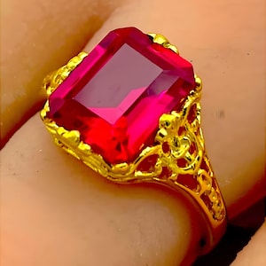 May include: A gold ring with a large, bright red, emerald-cut gemstone.