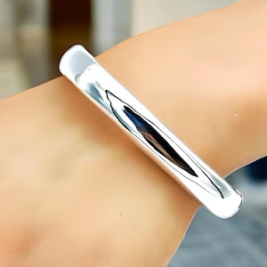 May include: A polished silver bangle bracelet with a smooth, rounded surface.