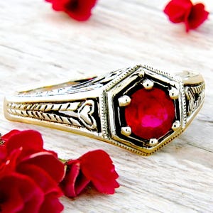 May include: A gold ring with an ornate design and a large, red gemstone in the center.
