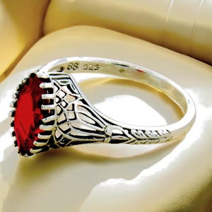 May include: A silver ring with a large, rectangular, red gemstone. The ring has an ornate, filigree design around the gemstone and on the band. The ring is marked with "SS 925".