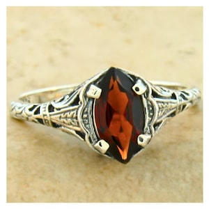 May include: A silver ring with an ornate filigree design and a marquise-shaped garnet gemstone.