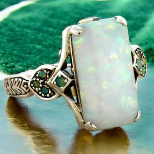 May include: A silver ring with a large rectangular white opal gemstone and smaller green gemstones set in the band.