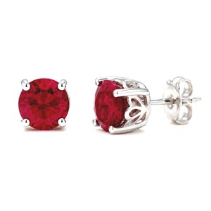 May include: A pair of stud earrings featuring round, faceted, deep red stones set in silver-toned metal. The settings have a decorative, open-work gallery design with four prongs holding each stone, and include standard silver-toned earring backs.