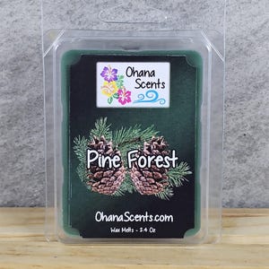 May include: A green wax melt with a pine forest scent. The wax melt is in a clear plastic container with a label that says "Ohana Scents" and "Pine Forest". The label also includes a small image of a pine tree and the website address "OhanaScents.com". The wax melt is 2.4 ounces.