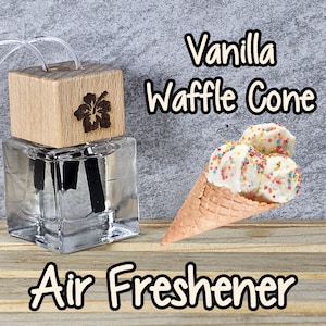 May include: A clear glass bottle with a wooden lid and a black diffuser stick. The bottle is filled with a clear liquid and has a floral design on the lid. The bottle is labeled "Vanilla Waffle Cone Air Freshener".