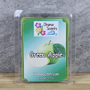 Puede incluir: Un fundente de cera con aroma a manzana verde en un envase de pl&aacute;stico transparente con forma de concha. El fundente de cera es verde y tiene una imagen de una manzana verde. La etiqueta dice "Ohana Scents" y "Green Apple". La etiqueta tambi&eacute;n dice "Wax Melts - 2.4 Oz".