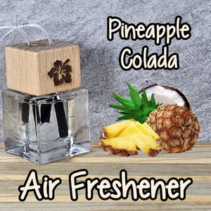 May include: A clear glass air freshener bottle with a wooden top, featuring a carved flower design. The words "Pineapple Colada" and "Air Freshener" are displayed. Pineapple slices, a coconut half, and pineapple leaves are also shown.