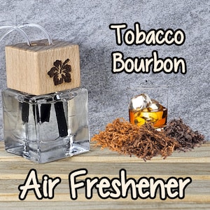May include: A clear glass bottle with a wooden lid and a black diffuser stick. The bottle is filled with a clear liquid and has a label that reads "Tobacco Bourbon Air Freshener". The bottle is sitting on a wooden surface with a pile of tobacco leaves and a glass of bourbon.