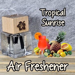May include: A glass bottle with a wooden lid and a hibiscus flower design. The bottle contains a clear liquid and two black reeds. The bottle is labeled "Tropical Sunrise Air Freshener". The image also shows a tropical drink and a variety of fruits.