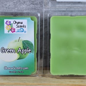 Puede incluir: Dos fundidos de cera en un envase de pl&aacute;stico transparente. El fundido de cera de la izquierda tiene una etiqueta que dice "Ohana Scents" y "Green Apple". El fundido de cera de la derecha es verde.