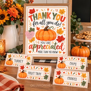 May include: A framed sign with the text THANK YOU for all you do! YOU ARE appreciated MORE THAN YOU KNOW! featuring a central orange pumpkin and autumn leaves. Four matching place cards labelled TURKEY, CHIPS, FRUIT TRAY, and COOKIES.