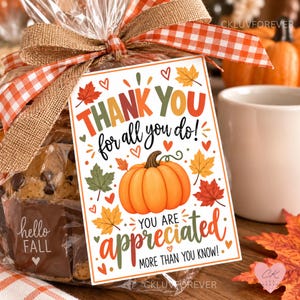 Puede incluir: Una etiqueta de regalo rectangular con fondo blanco que presenta una calabaza naranja, hojas de otoño coloridas y corazones rojos. El texto dice: THANK YOU for all you do! YOU ARE appreciated MORE THAN YOU KNOW! Atada con una cinta de cuadros naranja.