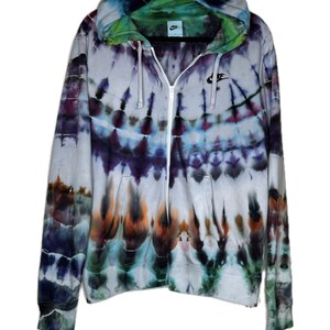 Pode incluir: Um moletom branco com z&iacute;per e um padr&atilde;o tie-dye em tons de azul, roxo, verde e laranja. O moletom tem um logotipo Nike preto no peito esquerdo.