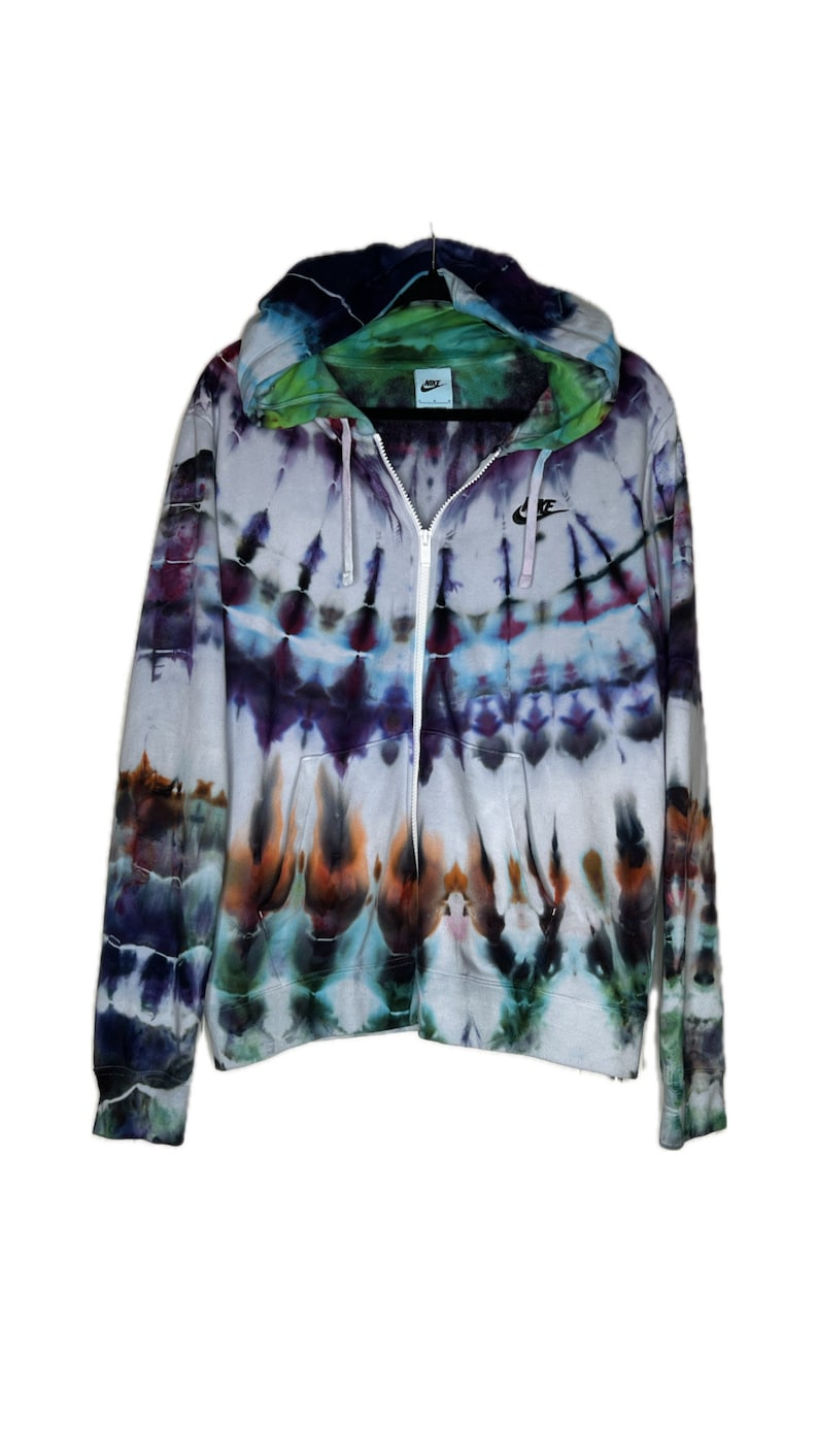 Pode incluir: Um moletom branco com z&iacute;per e um padr&atilde;o tie-dye em tons de azul, roxo, verde e laranja. O moletom tem um logotipo Nike preto no peito esquerdo.