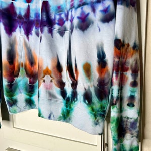 Pode incluir: Um moletom branco com z&iacute;per e um padr&atilde;o tie-dye em tons de azul, roxo, verde e laranja.