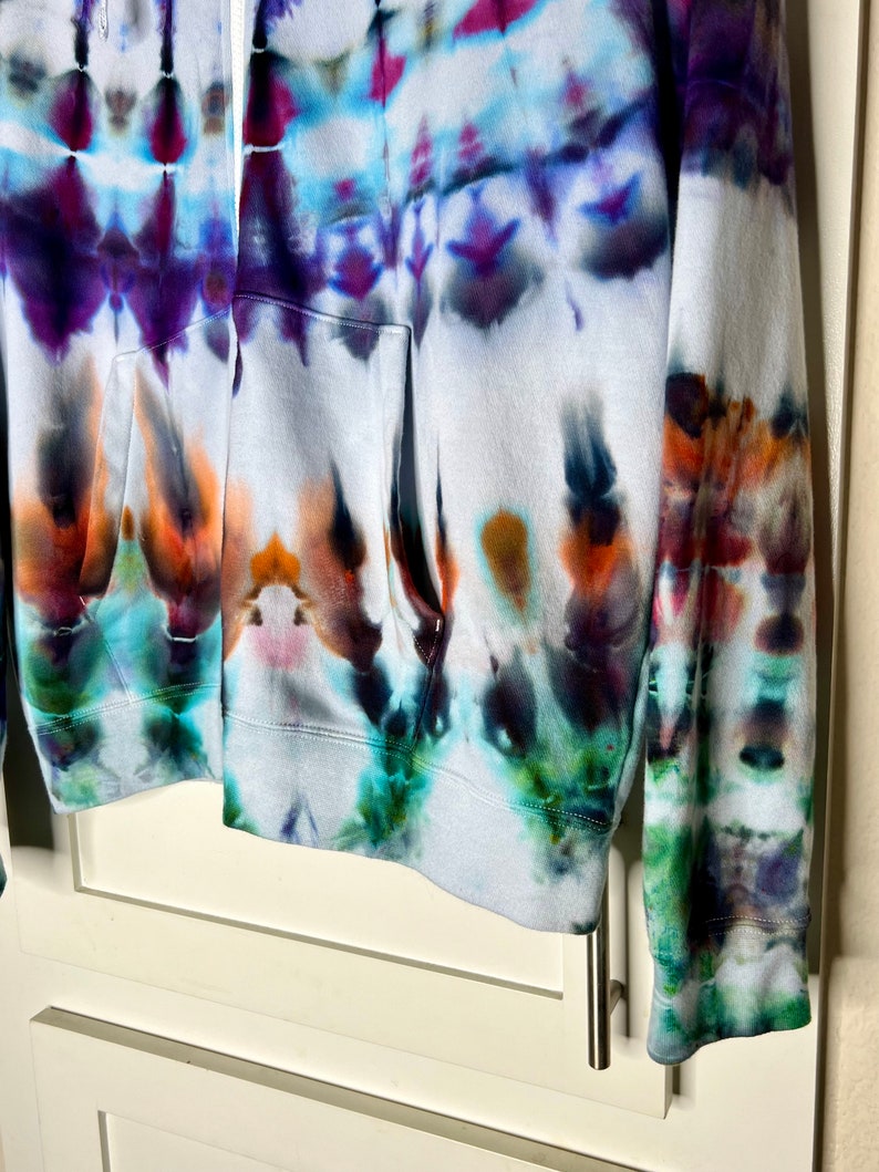 Pode incluir: Um moletom branco com z&iacute;per e um padr&atilde;o tie-dye em tons de azul, roxo, verde e laranja.