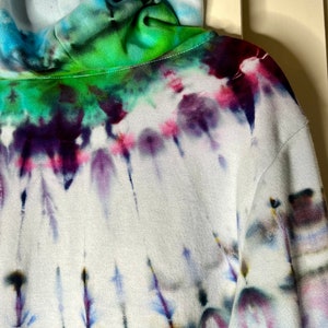 Pode incluir: Uma jaqueta de moletom branca com capuz com um padr&atilde;o tie-dye em tons de azul, verde, roxo e rosa.