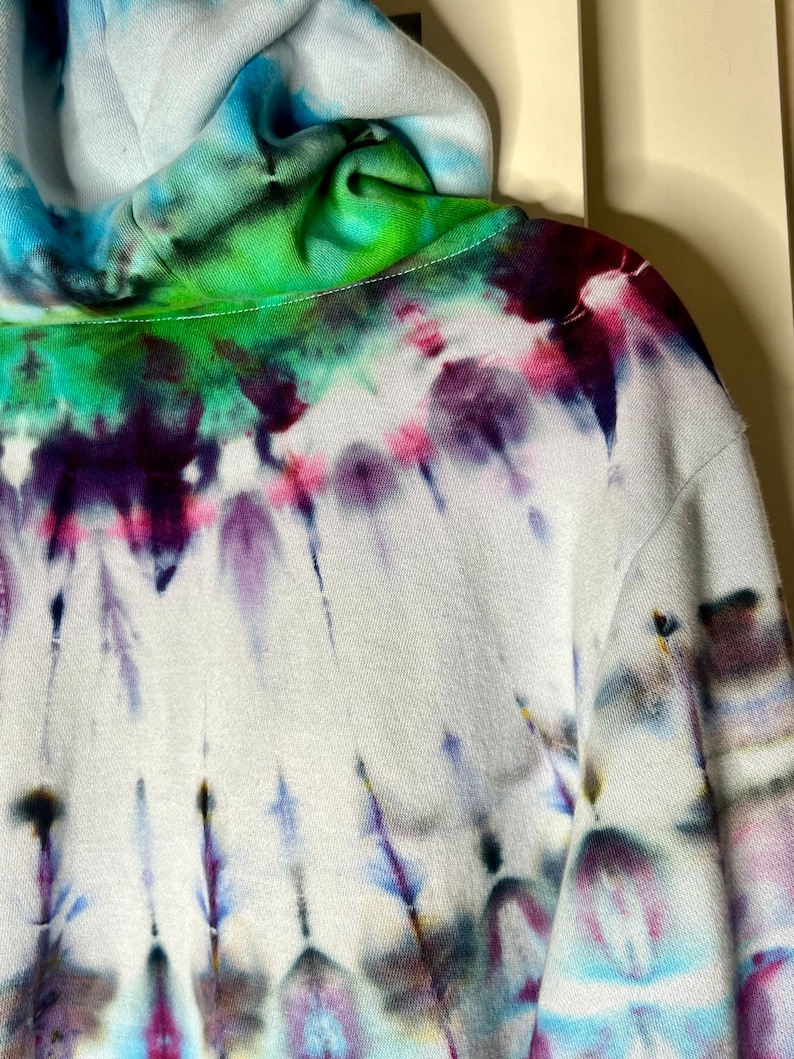 Pode incluir: Uma jaqueta de moletom branca com capuz com um padr&atilde;o tie-dye em tons de azul, verde, roxo e rosa.