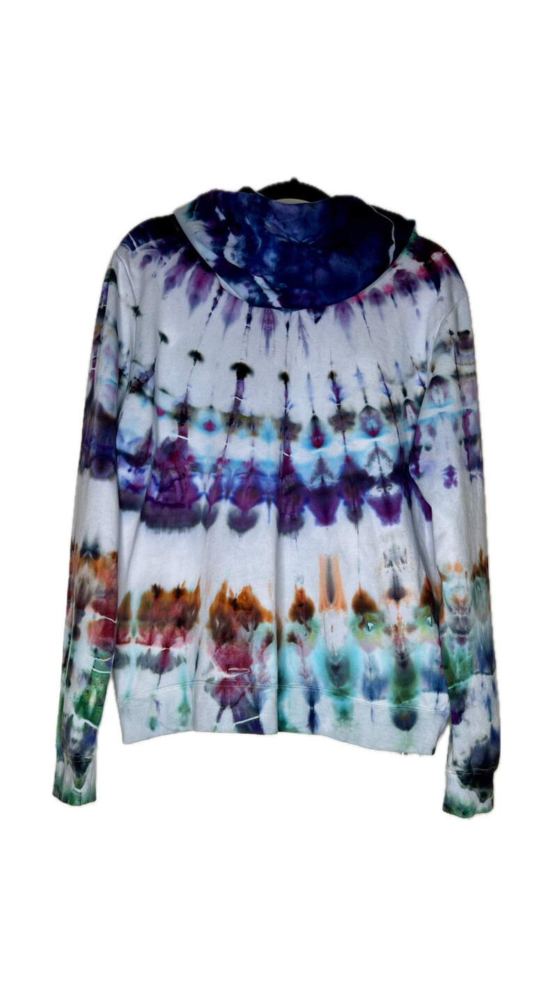 Pode incluir: Um moletom branco tie-dye com um padr&atilde;o azul, roxo e verde. O moletom tem capuz e mangas compridas.