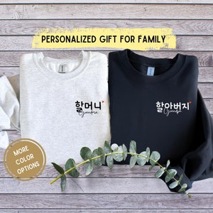 May include: Two sweatshirts, one light gray and one black, with Korean text and the English words "Grandma" and "Grandpa". The light gray sweatshirt has the word "Grandma" in Korean and English. The black sweatshirt has the word "Grandpa" in Korean and English. The text "PERSONALIZED GIFT FOR FAMILY" is at the top.