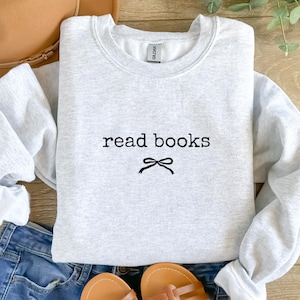 May include: A light gray sweatshirt with the words "read books" in black, with a small bow graphic underneath. The sweatshirt is a crew neck style and appears to be made of a soft material.