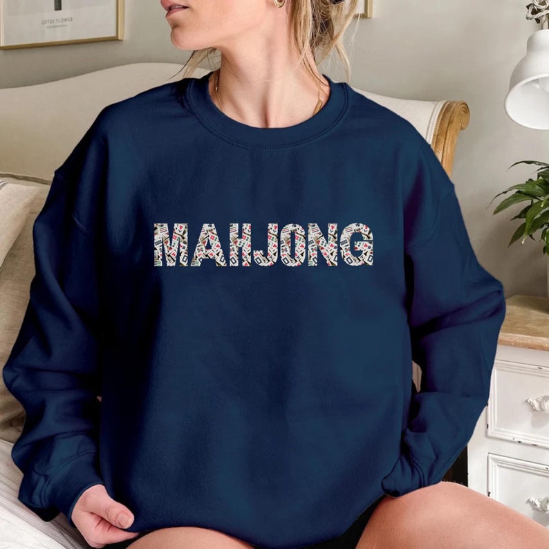 May include: A navy blue sweatshirt featuring the word "MAHJONG" in a patterned design. The letters are filled with images of mahjong tiles in red, white, and green. The sweatshirt has a crew neck.