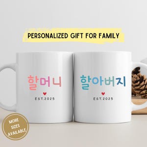 May include: Two white ceramic mugs with handles. The mug on the left has the Korean words "할머니" (grandmother) in pink and red lettering and the text "EST. 2025". The mug on the right has the Korean words "할아버지" (grandfather) in blue and green lettering and the text "EST. 2025".