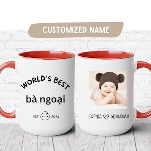 May include: White ceramic mug with a red interior and handle. The mug features the text "WORLD'S BEST bà ngoại" and a photo of a baby wearing a brown bear hat. The mug also has the text "EST. 2024" and "SOPHIA ♡ GRANDMA".