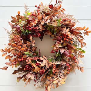 Peut inclure: Une couronne d'automne ornée de feuilles et de baies. La couronne présente un mélange de couleurs, notamment des nuances de marron, d'orange, de rouge et de vert. Les baies sont d'un rouge profond et les feuilles ont un aspect texturé. Fond blanc.
