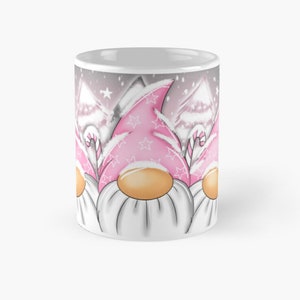 Peut inclure: Mug en céramique blanche avec une scène d'hiver représentant trois lutins portant des chapeaux roses avec des étoiles blanches. Les lutins ont des barbes blanches et se tiennent devant des arbres enneigés. L'arrière-plan est gris clair avec des flocons de neige blancs.