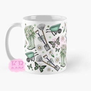 Può includere: Tazza in ceramica bianca con un design a tema giardino. Il design include illustrazioni di attrezzi da giardinaggio, farfalle, margherite e stivali di gomma pieni di fiori. La tavolozza dei colori comprende verde, bianco e grigio.