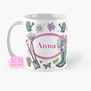 Può includere: Tazza in ceramica bianca con il nome "Anna" in rosa all'interno di una cornice ovale. La tazza è decorata con illustrazioni a tema giardinaggio, tra cui un annaffiatoio, fiori, un rastrello, una pala e una farfalla.