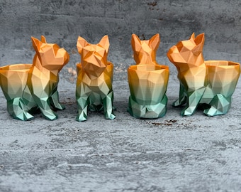 May include: Four small, geometric, ombre planter pots shaped like French Bulldogs. The pots are a gradient of orange, yellow, and green.