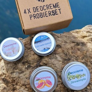 Könnte beinhalten: Eine braune Pappschachtel mit der Aufschrift 4 X DEOCREME PROBIERSET und einem Blattsymbol, dazu vier kleine runde silberne Metalldosen mit Deocreme. Jeder Dosendeckel trägt ein Etikett mit den Aufschriften Deocreme, Seide und Kaschmir, Duft nach Heimat, Blutorange und Zitronenmyrte.