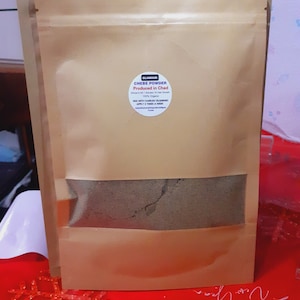 May include: A brown paper bag with a clear window showing a dark brown powder inside. The bag has a white label that says "GLAMOUR CHEBE POWDER Produced in Chad Africa's No.1 Solution To Hair Growth 100% Organic MIX WITH KARKAROL OIL & BRAD APPLY 2 TIMES A WEEK"
