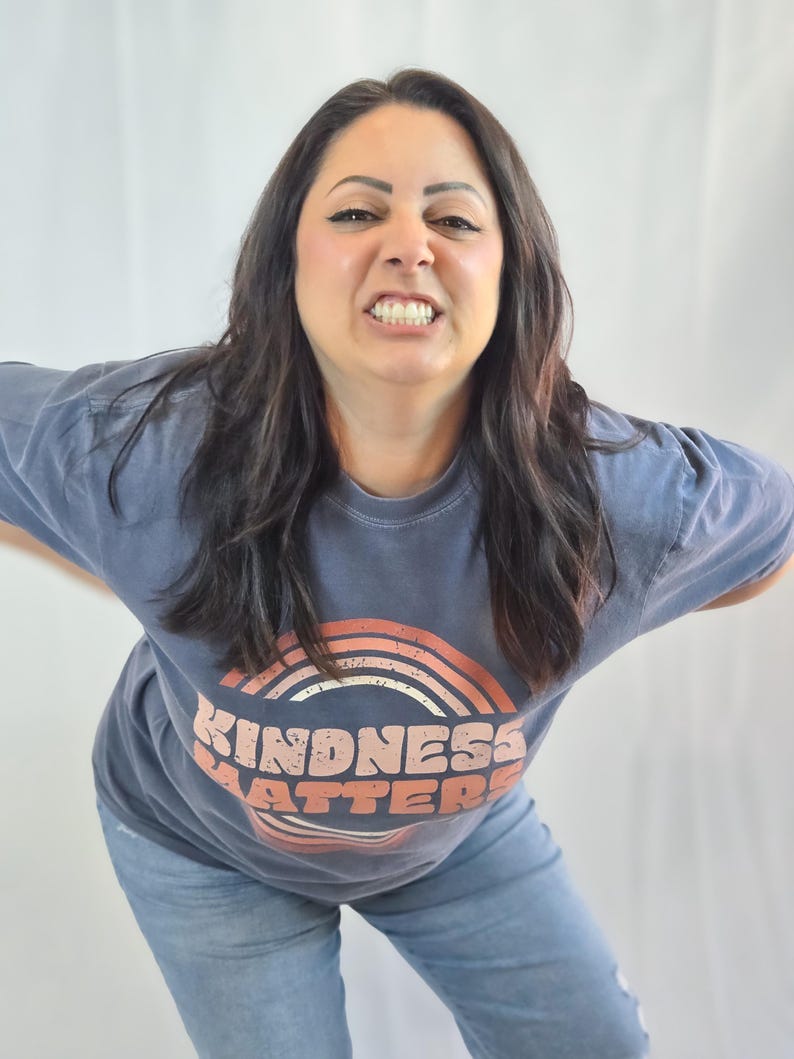Puede incluir: Una camiseta azul con el texto "KINDNESS MATTERS" en un dise&ntilde;o de arco&iacute;ris retro. Se combina con vaqueros azules claros. El estilo general es informal y c&oacute;modo.