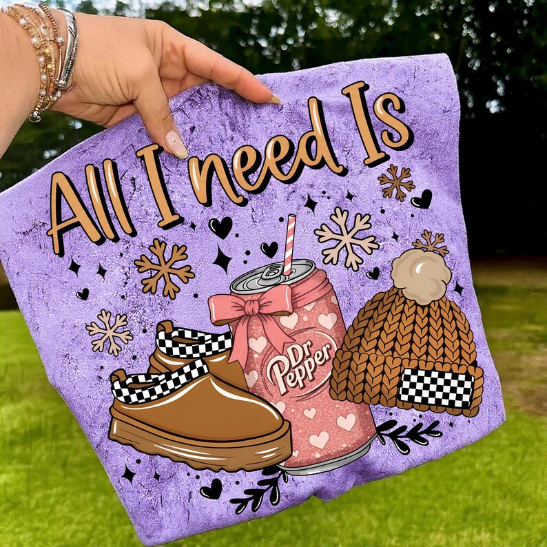May include: A purple graphic featuring the text "All I need Is" with illustrations of a Dr. Pepper can, a brown knit hat, and brown shoes with a black and white checkered pattern. The design includes snowflakes and hearts.