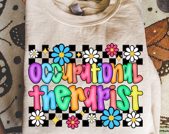 May include: A beige sweatshirt with the words "Occupational Therapist" in colorful bubble letters. The text is surrounded by a checkerboard pattern, daisies, and stars. The sweatshirt is folded.