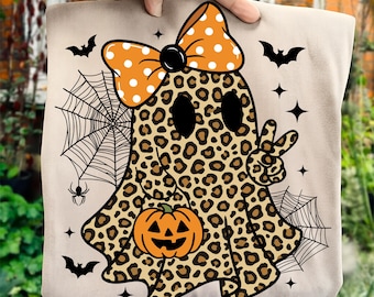 May include: A beige tote bag featuring a Halloween-themed design. The design includes a leopard print ghost with a pumpkin, an orange polka dot bow, bats, spiderwebs, and stars. The ghost is giving a peace sign.
