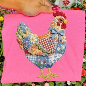 Peut inclure: Un t-shirt rose avec un motif de poulet patchwork. Le poulet a une cr&ecirc;te rouge, un bec jaune et un n&oelig;ud bleu. Le patchwork comprend des tissus floraux, &agrave; carreaux et &agrave; motifs. Les pattes du poulet sont jaunes.
