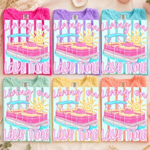 May include: Six colorful t-shirts with a graphic design featuring a pink pontoon boat, a sun, and the text "Living on Lake Time." The shirts are in various colors: pink, purple, blue, green, yellow, and orange.