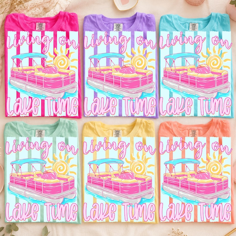 May include: Six colorful t-shirts with a graphic design featuring a pink pontoon boat, a sun, and the text "Living on Lake Time." The shirts are in various colors: pink, purple, blue, green, yellow, and orange.
