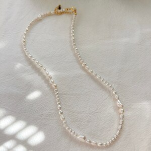 May include: A delicate pearl necklace with a gold clasp. The pearls are irregular in shape and size, giving the necklace a unique and natural look.